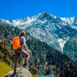 Man exploring breathtaking mountain scenery with snow-capped peaks under a clear blue sky.